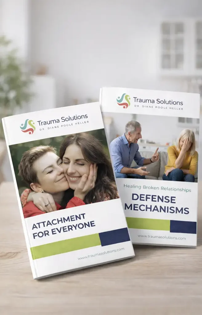 Two Trauma Solutions booklets titled “Attachment for Everyone” and “Defense Mechanisms” are displayed on a wooden surface.