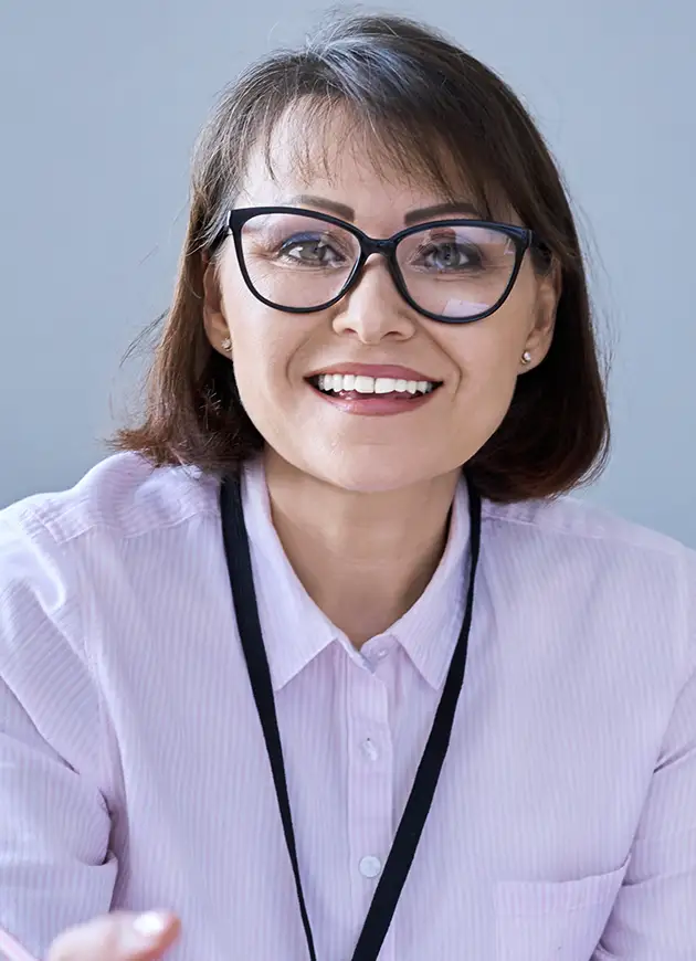 Woman with short brown hair and glasses, wearing a light purple collared shirt and a black lanyard, smiling at the camera against a plain background.