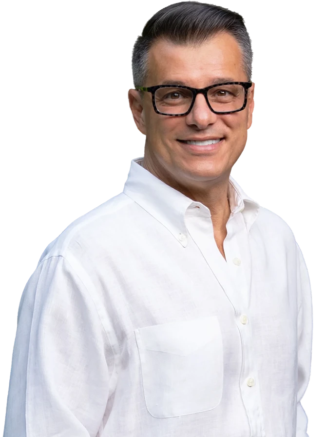 A man wearing black glasses and a white button-up shirt smiles while facing the camera.