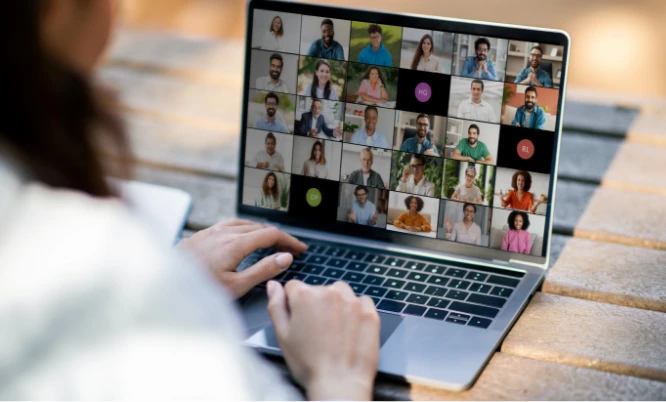 Person using a laptop to participate in a video conference with a group of people displayed in individual squares on the screen.